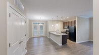 This one-bedroom, one-bathroom unit on Bluewater Way in Charleston, SC, is thoughtfully designed to maximize its single-floor layout. The open-concept living area seamlessly connects the kitchen, dining, and living spaces, creating an efficient and functional flow throughout.

The kitchen serves as a central feature, anchored by a peninsula-style island with granite countertops, an undermount double sink, and pendant lighting overhead. Dark espresso cabinetry contrasts with the light stone counters, while black appliances—including a refrigerator, electric range, and built-in microwave—complete the space. Recessed lighting and additional pendant fixtures provide ample illumination.

Wood-style flooring runs throughout the main living areas, lending a cohesive and clean aesthetic. The dining area adjoins the living space, which benefits from natural light through a set of French doors fitted with a transom window above, offering outdoor access and a bright, welcoming ambiance.

The bedroom is carpeted and equipped with a ceiling fan, a window for natural light, and access to a dedicated closet. A full bathroom, laundry area, and additional closet storage round out the layout, making this a well-appointed and practical single-level residence.