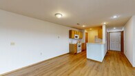 Located at 115 Pin Oak Dr in Aurora, Missouri, this single-floor, 2-bedroom, 2-bathroom home offers a functional and well-organized layout. Light wood-style flooring runs throughout the main living areas, creating a clean and cohesive aesthetic. The entry hallway leads into the heart of the home, with an electrical panel conveniently accessible near the entrance. The combined dining and kitchen area features warm honey-toned cabinetry, a white appliance suite including a range and built-in microwave, and a peninsula with counter seating that opens to the living space. The living room is generously sized and filled with natural light from a sliding glass door that provides outdoor access and views, complemented by a ceiling fan overhead. The two bedrooms are carpeted for comfort, with the primary bedroom offering a notably spacious footprint. Three closets, including a walk-in with wire shelving, provide ample storage throughout. Both bathrooms continue the wood-style flooring found in the main living areas. Additional practical spaces include a dedicated laundry room, a pantry, and a utility room, rounding out this well-appointed single-level home.