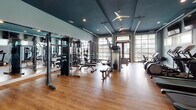 Located at 7111 Rock Fish Ln in Wilmington, NC, this single-floor fitness center is a comprehensive facility designed to support a wide range of workout routines. The space is immediately distinguished by its bold teal-painted ceilings, light blue walls, and warm hardwood-style flooring, creating an energizing yet welcoming atmosphere throughout.

The main cardio and strength area is generously proportioned, housing a full lineup of Precor equipment including treadmills, elliptical trainers, stationary bikes, and cable weight machines. Wall-mounted flat-screen televisions line one side of the room, while large garage-style windows flood the space with natural light and offer views of the outdoors. Ceiling fans provide additional airflow and comfort during workouts.

A dedicated studio space serves multiple fitness disciplines. It features a wall-length mirror, a classic wooden ballet barre, and open floor space suitable for group classes, stretching, or functional training. A multi-functional rack stocked with dumbbells, TRX suspension trainers, and resistance tools provides versatile training options. Adjacent to this, a spinning studio houses a row of Spinning-brand bikes positioned in front of tall windows dressed with horizontal blinds, offering a bright and focused cycling environment.

Together, the areas of this fitness center provide a thorough and thoughtfully designed workout destination.