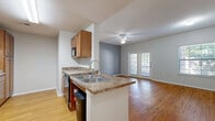 This single-story, 3-bedroom, 2-bathroom home offers a thoughtfully designed layout that maximizes functionality and comfort. The open-concept kitchen and living area serves as the heart of the home, where warm hardwood-style flooring flows throughout. The kitchen features rich wood cabinetry, granite-style countertops, a peninsula with a double sink, and a full suite of black appliances including a refrigerator, range, dishwasher, and microwave. The spacious living room is bathed in natural light courtesy of a large window and a set of classic French doors, which also provide outdoor access. A ceiling fan adds to the room's comfort. The primary bedroom is a generous retreat with hardwood-style flooring and direct access to a private room, while the additional bedrooms offer plush carpeting, ceiling fans, and natural light from exterior windows with closet storage. The two bathrooms are functionally designed, each featuring a tiled tub-shower combination with a curved curtain rod, hardwood-style flooring, and clean white finishes. One bathroom is equipped with accessibility grab bars. A connecting hallway ties all areas of the home together for a cohesive and efficient floor plan.