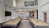 Located at 3000 Bissonnet St in Houston's desirable 77005 area, this single-floor amenity space is designed to offer residents a well-rounded social and recreational environment. The centerpiece is a spacious billiards lounge featuring soaring double-height ceilings, two full-size pool tables, and a shuffleboard table. Arched architectural details and an open mezzanine above lend the room a grand, airy feel, while large glass doors invite natural light and offer direct access to the outdoors.

Adjacent to the game room, a comfortable lounge area provides casual seating alongside a wall-mounted flat-screen TV and stylish decorative accents. A sleek kitchenette nearby is outfitted with a coffee station, under-counter refrigerator, and a striking mosaic tile accent wall that adds a bold design element.

The library and conference area features floor-to-ceiling built-in bookshelves stocked with a curated collection, a glass-top conference table with upholstered seating, and carefully placed artwork, creating a refined and focused atmosphere. A separate media nook rounds out the space with additional seating and a wall-recessed television. The business center, accessible through glass-paned doors, provides a bright and professional workspace with ample natural light. Throughout, the design maintains a cohesive contemporary aesthetic with neutral tones, tile flooring, and thoughtful lighting.