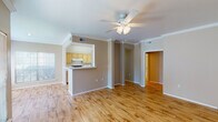 Located in College Station, Texas, this single-story unit offers a practical and well-organized floor plan with a cohesive design throughout. The open living area is finished with warm hardwood flooring that extends through the main living spaces, complemented by crown molding and a ceiling fan with integrated lighting. Large windows allow natural light to fill the room, creating a bright and inviting atmosphere. A pass-through peninsula connects the living area to the galley-style kitchen, which features light wood cabinetry, white appliances including a refrigerator, electric range, microwave, and dishwasher, along with hardwood flooring and ample counter space on both sides. A dedicated laundry closet with a stacked washer and dryer unit is conveniently accessible directly from the kitchen. The bedrooms are carpeted for comfort and each includes a ceiling fan and window with natural views. The bathroom is outfitted with white tile surrounding a full soaking tub and shower combination, wood cabinetry for storage, and accessibility grab bars for added safety and convenience. The overall ambiance is clean, functional, and move-in ready.