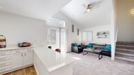 This two-floor residence is designed with an open, airy layout that maximizes natural light and functionality. The main living area impresses with soaring vaulted ceilings and a ceiling fan, creating a spacious and comfortable atmosphere. Large sliding glass doors open to a private balcony, flooding the living space with greenery views and natural light. The carpeted living room provides a welcoming setting, while the adjacent kitchen features white shaker cabinetry, light quartz countertops, a built-in pantry with open shelving, hardwood-style flooring, and a peninsula with bar seating — ideal for casual dining or entertaining. A high transom window above the balcony doors further enhances the sense of openness. The bedrooms are carpeted and thoughtfully designed, each equipped with a ceiling fan and a built-in closet. One bedroom includes a built-in desk area positioned beneath a bright window, offering a dedicated study nook. The bathroom presents a clean, modern aesthetic with white cabinetry, quartz countertops, and hardwood-style flooring. Throughout the space, a consistent white-and-neutral palette contributes to a bright, cohesive, and inviting ambiance.