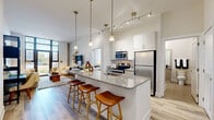 Located at 10902 Georgia Ave in Silver Spring, MD, this well-appointed one-bedroom, one-bathroom residence offers a thoughtfully designed open-concept layout with modern finishes throughout. Light-toned hardwood flooring flows through the main living areas, enhancing the bright, airy atmosphere created by the high ceilings and abundant natural light.

The kitchen serves as the centerpiece of the space, featuring a large granite-topped island with seating for multiple guests, crisp white cabinetry, stainless steel appliances — including a refrigerator, range, and microwave — and pendant lighting overhead. Track lighting adds additional illumination throughout.

The living room is anchored by floor-to-ceiling windows that fill the room with natural light and offer outdoor views, creating a seamless connection to the exterior. The space is generous enough to comfortably accommodate a full seating arrangement.

The spacious primary bedroom features plush carpeting, large windows with outdoor views, and ample room for a full furniture set. A dedicated closet provides convenient storage.

The bathroom is finished with tile flooring, a granite-topped vanity, and a full tub-shower combination. A separate closet completes the unit's practical layout, making this an efficient and stylish residence in a modern building.