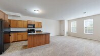 Located at 104 Merchant Ave in Mount Joy, PA, this single-floor residence offers a practical and comfortable layout with two bedrooms and two full bathrooms. The open-concept kitchen and living area forms the heart of the home, where warm honey-toned cabinetry, dark countertops, and a central kitchen island with a built-in sink create a functional yet inviting space. Black appliances, including a refrigerator, electric range, and microwave, complement the kitchen's clean aesthetic. Tile flooring grounds the kitchen area, transitioning seamlessly into plush wall-to-wall carpeting throughout the living and bedroom spaces. The spacious living room is bathed in natural light through a trio of large windows, lending an airy, open feel to the space. The primary bedroom is generously sized, featuring dual windows, soft carpeting, a closet, and direct access to a private en-suite bathroom equipped with a walk-in shower. The second bedroom is well-proportioned, also featuring carpeted floors and a window for natural light. The second full bathroom offers a tub-shower combination, a wood-toned vanity, and tile flooring, maintaining the home's consistent, clean design language throughout.
