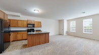 Located at 104 Merchant Ave in Mount Joy, PA, this single-floor residence offers a practical and comfortable layout with two bedrooms and two full bathrooms. The open-concept kitchen and living area forms the heart of the home, where warm honey-toned cabinetry, dark countertops, and a central kitchen island with a built-in sink create a functional yet inviting space. Black appliances, including a refrigerator, electric range, and microwave, complement the kitchen's clean aesthetic. Tile flooring grounds the kitchen area, transitioning seamlessly into plush wall-to-wall carpeting throughout the living and bedroom spaces. The spacious living room is bathed in natural light through a trio of large windows, lending an airy, open feel to the space. The primary bedroom is generously sized, featuring dual windows, soft carpeting, a closet, and direct access to a private en-suite bathroom equipped with a walk-in shower. The second bedroom is well-proportioned, also featuring carpeted floors and a window for natural light. The second full bathroom offers a tub-shower combination, a wood-toned vanity, and tile flooring, maintaining the home's consistent, clean design language throughout.