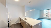 Located in Chicago's vibrant Lincoln Park neighborhood, this modern one-bedroom, one-bathroom residence offers a sleek, contemporary design with high-quality finishes throughout. The open-concept living and kitchen area is anchored by wide-plank hardwood flooring and clean white walls, creating a bright and airy atmosphere. Floor-to-ceiling windows and a glass-panel balcony door flood the living space with natural light while framing expansive views of the surrounding cityscape.

The kitchen is thoughtfully designed with warm wood-grain cabinetry, white quartz countertops, stainless steel appliances including a gas range and refrigerator, and a peninsula with an undermount sink — ideal for both cooking and casual dining. A modern linear pendant light adds a refined touch overhead.

The bedroom is a well-proportioned retreat featuring large windows and a private balcony access, offering sweeping views of the Chicago skyline and neighborhood rooftops. Dark hardwood floors contrast elegantly with the crisp white walls throughout.

The bathroom is finished with large-format light tile, a frameless glass walk-in shower with a handheld fixture, and a wood-vanity with an undermount sink, maintaining the home's cohesive modern aesthetic. The overall design emphasizes clean lines, natural materials, and an abundance of light.