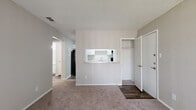 This well-organized single-floor unit offers a practical and comfortable layout across five distinct spaces: a living area, kitchen, bedroom, bathroom, and closet — all connected via a central hallway. The living area is carpeted and filled with natural light through a large sliding glass door fitted with vertical blinds, offering an outdoor view of surrounding greenery. A textured popcorn ceiling and neutral warm-gray walls give the space a consistent, understated aesthetic throughout.

The kitchen features a pass-through window with a light granite-style countertop that opens directly to the living area, creating an open and connected feel. White cabinetry with sleek silver hardware, a black electric range with overhead exhaust, a black refrigerator, and wood-look vinyl flooring complete the kitchen's functional design.

The bedroom is a comfortable, carpeted retreat equipped with a ceiling fan with light fixture and a window that invites natural light and outdoor views. A dedicated closet provides additional storage convenience.

The bathroom is finished with the same wood-look vinyl flooring as the kitchen and includes a white vanity with granite-style countertop, an undermount sink, a combined tub and shower with tiled surround, and clean white fixtures throughout. The overall unit presents a clean, move-in-ready aesthetic with consistent finishes across all rooms.