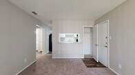 This well-organized single-floor unit offers a practical and comfortable layout across five distinct spaces: a living area, kitchen, bedroom, bathroom, and closet — all connected via a central hallway. The living area is carpeted and filled with natural light through a large sliding glass door fitted with vertical blinds, offering an outdoor view of surrounding greenery. A textured popcorn ceiling and neutral warm-gray walls give the space a consistent, understated aesthetic throughout.

The kitchen features a pass-through window with a light granite-style countertop that opens directly to the living area, creating an open and connected feel. White cabinetry with sleek silver hardware, a black electric range with overhead exhaust, a black refrigerator, and wood-look vinyl flooring complete the kitchen's functional design.

The bedroom is a comfortable, carpeted retreat equipped with a ceiling fan with light fixture and a window that invites natural light and outdoor views. A dedicated closet provides additional storage convenience.

The bathroom is finished with the same wood-look vinyl flooring as the kitchen and includes a white vanity with granite-style countertop, an undermount sink, a combined tub and shower with tiled surround, and clean white fixtures throughout. The overall unit presents a clean, move-in-ready aesthetic with consistent finishes across all rooms.