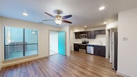This single-floor unit offers a thoughtfully designed open-concept layout that seamlessly connects the living and kitchen areas. Warm hardwood-style flooring runs throughout, complementing the clean white walls and recessed lighting that keep the space feeling bright and inviting. Ceiling fans in the main living areas provide both comfort and a finishing touch to the design.

The kitchen is a standout feature, outfitted with rich dark cabinetry, white countertops, and a full suite of stainless steel appliances including a refrigerator, range, microwave, and dishwasher. A stacked in-unit washer and dryer is conveniently tucked just off the kitchen, adding a practical touch to everyday living.

The bedroom is generously sized, bathed in natural light from a large window with blinds, and continues the same warm flooring found throughout the unit. A vibrant teal front door makes for a welcoming entryway with character.

The bathroom is cleanly appointed with a dark-framed vanity mirror, dark cabinetry, a white countertop with an undermount sink, and chrome fixtures. A shower-tub combo completes the space. Overall, this unit balances modern finishes with functional design, creating a comfortable and cohesive living environment.