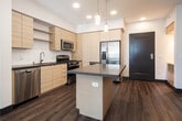 Located at 1800 E Gene Autry Way in Anaheim, California, this single-floor residence showcases a thoughtfully designed contemporary interior with a clean, modern aesthetic throughout. The kitchen serves as a central highlight, featuring light wood cabinetry, open shelving, and a full suite of stainless steel appliances including a gas range, built-in microwave, dishwasher, and a French door refrigerator. A center island with a quartz-style countertop provides additional prep space and is illuminated by stylish pendant lighting. Wood-look plank flooring runs throughout the kitchen and living areas, adding warmth and continuity. The bedrooms are finished with plush carpet, ceiling fans with integrated lighting, and dark-framed doors that provide a modern contrast to the neutral walls. At least one bedroom features direct access to a walk-in closet with built-in shelving. The bathroom is well-appointed with a wide vanity, large wall mirror, contemporary light fixtures, and a full tub-shower combination with a clean tile surround. Recessed lighting and a neutral color palette create a bright, cohesive ambiance throughout the entire space.