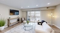 Located at 1710 Devonshire Rd in Hauppauge, NY, this well-appointed one-bedroom, one-bathroom unit offers a thoughtfully designed layout across a single floor. The open-concept living and kitchen area serves as the heart of the home, featuring light hardwood-style flooring, recessed lighting, and a large sliding glass door that floods the space with natural light and provides access to the outdoors. The kitchen is efficiently designed with white shaker cabinetry, marble-style countertops, stainless steel appliances including a range, microwave, and refrigerator, and a peninsula with pendant lighting that doubles as a breakfast bar. The living room offers a comfortable, airy atmosphere with recessed lighting and a wall-mounted TV area. The bedroom is carpeted for warmth and comfort, includes a ceiling fan, a built-in closet, and a window with outdoor views. A hallway connects the main living areas to the full bathroom, which is finished with large-format tile surrounding a soaking tub and shower, a marble-top vanity, and clean, neutral tones throughout. The overall aesthetic is modern and cohesive, with a neutral palette that enhances the sense of openness throughout the unit.
