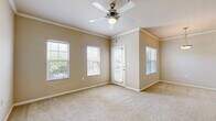 This single-floor, one-bedroom, one-bathroom residence offers a thoughtfully designed layout that makes efficient use of its space. The living area is bright and welcoming, featuring plush wall-to-wall carpeting, warm neutral-toned walls, and elegant crown molding that adds a refined architectural detail. Multiple windows dressed with horizontal blinds allow generous natural light to fill the room, while a ceiling fan with a built-in light fixture provides both comfort and illumination. A private door opens directly to an outdoor balcony, further enhancing the airy feel of the main living space.

The kitchen is equipped with warm wood-toned cabinetry, dark granite-style countertops, and a full suite of black appliances including a refrigerator, range, microwave, and dishwasher. A peninsula with an integrated sink serves as a functional divider between the kitchen and living area, and pendant lighting overhead adds a stylish touch. Wood-style flooring grounds the kitchen zone distinctly from the carpeted areas.

The bedroom is a comfortable, carpeted retreat with a ceiling fan and natural light from windows with blinds. A dedicated closet provides valuable storage. The bathroom features tile flooring, a combined tub and shower, a wood-toned vanity with granite-style countertops, and a large mirror.