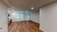 This single-floor unit presents a clean, modern aesthetic defined by warm hardwood-style flooring that runs consistently throughout every room, complementing the neutral gray and white wall tones. Recessed lighting is installed across the unit, providing even, functional illumination in each space.

The open living area is generously proportioned, featuring a bank of windows dressed with horizontal blinds that allow for adjustable natural light. The layout accommodates both a living and dining arrangement comfortably.

The kitchen is efficiently designed with a linear configuration, offering warm wood-toned cabinetry in both upper and lower configurations, a white countertop, tile backsplash, and a full suite of stainless steel appliances including a refrigerator, electric range, over-the-range microwave, and dishwasher.

The unit includes two private rooms, each with hardwood-style flooring, recessed lighting, and windows with blinds. Two bathrooms mirror each other in design, each featuring wood-toned vanity cabinetry, a white countertop with an undermount sink, a large mirror, and hardwood-style flooring. In-unit stacked laundry is also present, adding everyday convenience to this well-appointed space.