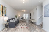 This two-floor home offers a thoughtfully designed layout with consistent, modern finishes carried throughout every level. The main living area is open and elongated, featuring light hardwood-style flooring, crisp white walls, and a colorful abstract art piece that adds a vibrant focal point. The space flows naturally into a dining area, which is bathed in natural light from a glass-paneled door. The kitchen is well-equipped with dark espresso cabinetry, granite-style countertops, a mosaic tile backsplash, and a full suite of stainless steel appliances, including a French door refrigerator and electric range. A window above the sink provides additional natural light. The bedrooms are comfortably sized, each featuring the same rich wood-tone flooring and large windows dressed with sheer white curtains that allow soft light to filter in. The primary bedroom includes a pendant light fixture and an ornate wall mirror, adding warmth and character. The bathrooms are clean and functional, featuring white vanities, large mirrors, and a tub-shower combination. An additional flex room with neutral walls and a single window offers versatile use as a home office or guest space. The overall ambiance is bright, clean, and move-in ready.