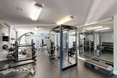 Located at 250 S Whiting St in Alexandria, Virginia, this fitness center offers a well-appointed exercise space spread across a single floor. The layout is thoughtfully organized into distinct zones, allowing for both strength training and cardiovascular workouts without overcrowding.

The strength training area is a standout feature, equipped with a Jones/Bodycraft power rack, multiple barbell and dumbbell racks stocked with a full range of weights, a multi-station functional cable trainer, and various benches and selectorized machines. Floor-to-ceiling mirrors line portions of the walls, enhancing the sense of openness and allowing users to monitor their form during workouts.

The cardio zone is equally well-furnished, featuring treadmills, stair climbers, stationary bikes, rowing machines, and elliptical trainers. This section benefits from large sliding glass doors that open toward an outdoor pool area, allowing natural light to flood in and providing pleasant outdoor views.

The space features durable rubber flooring in the weight areas and patterned multi-tone carpet-style flooring in the cardio sections, contributing to both functionality and visual interest. Bright overhead fluorescent and recessed lighting ensures excellent visibility throughout. Stability balls and additional accessories are available, rounding out a comprehensive fitness offering suited to a wide variety of training needs.