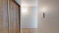 Located at 240 2nd Ave SE in Milaca, Minnesota, this one-bedroom, one-bathroom unit offers a straightforward single-floor layout designed for comfortable, efficient living. The main living area features warm beige carpeting, light gray walls, and a textured ceiling, giving the space a clean and neutral aesthetic. A large wood-framed window allows natural light to fill the room, with a baseboard heating system running along the walls to ensure warmth throughout the seasons. The bedroom is a well-proportioned space with matching carpet and a wood-trimmed window that brings in natural light, creating a bright and restful atmosphere. Warm-toned wood doors add a classic touch to the interior. The kitchen is equipped with wood cabinetry, a white refrigerator, and a range, providing all the essential amenities within a compact and functional arrangement. A hallway connects the main living areas and leads to the bathroom, which features a walk-in shower unit with stainless steel grab bars and a handheld showerhead, making it both practical and accessibility-friendly. Throughout the unit, the design remains consistent with neutral tones and straightforward finishes, creating a cohesive and livable environment suited for those seeking a manageable, low-maintenance space in Milaca, MN.