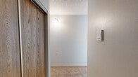 Located at 240 2nd Ave SE in Milaca, Minnesota, this one-bedroom, one-bathroom unit offers a straightforward single-floor layout designed for comfortable, efficient living. The main living area features warm beige carpeting, light gray walls, and a textured ceiling, giving the space a clean and neutral aesthetic. A large wood-framed window allows natural light to fill the room, with a baseboard heating system running along the walls to ensure warmth throughout the seasons. The bedroom is a well-proportioned space with matching carpet and a wood-trimmed window that brings in natural light, creating a bright and restful atmosphere. Warm-toned wood doors add a classic touch to the interior. The kitchen is equipped with wood cabinetry, a white refrigerator, and a range, providing all the essential amenities within a compact and functional arrangement. A hallway connects the main living areas and leads to the bathroom, which features a walk-in shower unit with stainless steel grab bars and a handheld showerhead, making it both practical and accessibility-friendly. Throughout the unit, the design remains consistent with neutral tones and straightforward finishes, creating a cohesive and livable environment suited for those seeking a manageable, low-maintenance space in Milaca, MN.