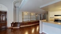 Located at 115 Monument Ave in Dayton's historic Monument Avenue district, this two-story loft offers a distinctive architectural character that sets it apart. The main level features rich hardwood flooring throughout, soaring ceilings with clerestory windows that flood the space with natural light, and a standout raised platform area framed by a curved, dark-wood fascia with decorative tile accents — a dramatic architectural centerpiece. Extensive built-in shelving lines the living area walls, offering generous display and storage capacity. The open-concept kitchen is well-appointed with white cabinetry, stone-topped counters, stainless steel appliances, and a pass-through breakfast bar that connects seamlessly to the living space. A half bathroom on the main level features hardwood flooring and a stone-topped vanity. The upper level is accessed via a staircase and opens to a carpeted loft space illuminated by multiple skylights, with an arched wall detail and an open railing overlooking the floor below. This level includes a dedicated closet and a full bathroom complete with a tiled tub-shower combination. Together, both levels deliver a well-balanced, architecturally rich living environment with abundant character.