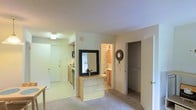 This compact apartment showcases an efficient open-concept design that maximizes space utilization. The layout seamlessly integrates various living areas within a single floor. Upon entry, a small kitchen area is visible to the left, equipped with essential appliances and cabinetry. The kitchen's light-colored surfaces contribute to a sense of openness.

Adjacent to the kitchen, a central space serves as a hub, potentially functioning as a living or dining area. A notable feature is a built-in wooden structure with a large square mirror, which may serve as a vanity or decorative element while visually expanding the space.

To the right, a glimpse of the bathroom is visible, featuring what appears to be a tiled shower area. The bathroom's warm lighting creates an inviting ambiance. Next to the bathroom, a closet or storage area provides additional functionality.

The apartment's neutral color palette, dominated by light tones on walls and ceilings, enhances the sense of spaciousness. Carpeted flooring in the main area adds warmth and comfort. Recessed lighting and a central ceiling fixture ensure well-distributed illumination throughout the space.

This thoughtfully designed apartment efficiently combines essential living areas, making it ideal for those seeking a cozy, low-maintenance living space in an urban setting.