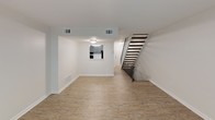 This three-floor home offers a well-organized layout with distinct living areas spread across each level. The main floor serves as the central hub, featuring an open living area with light hardwood-style flooring and a sliding glass door fitted with vertical blinds that invites natural light. Adjacent to the living space, the kitchen is outfitted with gray cabinetry, light stone-look countertops, a subway tile backsplash, a stainless steel sink, and black appliances including a gas range. A staircase with a sleek metal railing connects the main floor to the upper and lower levels.

The upper floor hosts multiple bedrooms finished with plush neutral carpeting and windows with blinds that provide ample natural light. One bedroom features a double-door closet and additional access to neighboring rooms, offering flexible use of space. A full bathroom on this level includes a tiled tub-and-shower combination with brushed nickel fixtures and a vanity with a large mirror.

The lower level presents a finished open room with dark hardwood-style flooring and ground-level windows, making it a versatile space for recreation or additional living. A bathroom with a vanity and toilet completes this floor.