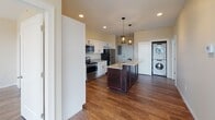 Located at 1909 Atchison Ave in Whiting, Indiana, this single-floor unit offers a thoughtfully designed layout with modern finishes throughout. Rich hardwood-style flooring runs continuously through the main living areas, establishing a cohesive and polished aesthetic.

The kitchen serves as a central highlight, featuring white shaker-style cabinetry with matte black hardware, granite countertops, and a full suite of stainless steel appliances including a refrigerator, electric range, and over-the-range microwave. A dark-baselined island with a light granite top provides additional prep space and seating, illuminated by two pendant lights overhead. Recessed lighting adds to the bright, functional atmosphere. Conveniently situated nearby, a stacked washer and dryer unit is tucked into a dedicated alcove, keeping laundry within easy reach.

The bedrooms are well-proportioned, each equipped with ceiling fans, closets, and large windows that invite natural light and offer elevated views of the surrounding Whiting neighborhood. The bathrooms are finished with granite-topped vanities and white cabinetry. The primary bath includes a glass-enclosed walk-in shower, while the secondary bath offers a clean, compact design with warm accent wall tones and stylish lighting.