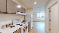 Located at 2133 North Argyle Street in Portland, Oregon, this efficiently designed studio unit offers a practical and well-organized single-floor layout. The combined kitchen and living area makes smart use of the available space, with the kitchen positioned along one wall and the open living area extending toward a large window that fills the room with natural light and offers views of the surrounding neighborhood. The kitchen is fully equipped with white appliances, including an electric range with overhead ventilation, a full-size refrigerator, and a dishwasher. Rich, dark-toned cabinetry provides ample storage above and below the clean white countertops. Light wood-look flooring runs throughout the entire unit, lending warmth and visual continuity from the kitchen through the living area. A ceiling fan with integrated lighting serves the living space, contributing to both comfort and ambiance. The bathroom features a full tub-shower combination with clean white surroundings, wood-look flooring consistent with the rest of the unit, and a vanity with matching cabinetry. Recessed lighting and a neutral color palette throughout keep the space feeling bright, clean, and open. A dedicated entryway with a closet provides additional storage and a clear transition into the living area.