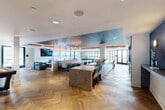 Located along Philadelphia's waterfront at 501 North Christopher Columbus Boulevard, this generously sized amenity lounge offers a sophisticated and multifunctional gathering space across a single, open floor. The interior is anchored by striking herringbone-patterned hardwood floors that flow seamlessly throughout, tying together distinct activity zones with a cohesive, upscale aesthetic.

The main lounge area features a dramatic marble fireplace surround paired with a wall-mounted television and refined seating arrangements. A tray ceiling with warm wood accents adds architectural depth, while recessed lighting and pendant fixtures in brass tones lend a polished finish. An expansive bar and dining counter with teal upholstered seating serves as a central social hub, complemented by a darkened ceiling detail that defines the space.

A dedicated game area includes a full-size billiards table set atop a bold area rug, an arcade cabinet, and built-in shelving, catering to a lively atmosphere. Floor-to-ceiling glass doors and large windows flood the interior with natural light and provide direct access to two generous outdoor terraces. These covered outdoor areas offer panoramic views of the Delaware River and the Benjamin Franklin Bridge, furnished with lounge seating for relaxed outdoor enjoyment. The combination of refined interiors and exceptional waterfront views makes this a standout communal destination.