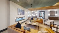 Located at 125 River Birch Grove Rd. in Asheville, NC, this single-floor amenity space masterfully combines rustic mountain character with contemporary design sensibilities. Exposed natural wood ceiling beams run throughout the open layout, creating a warm, cohesive aesthetic that ties the entire space together.

The kitchen area is a standout feature, showcasing a large central island with a crisp white quartz countertop and seating for multiple guests. Deep navy cabinetry with gold hardware lines the walls, complemented by a textured gray subway tile backsplash and open black metal shelving. Stainless steel appliances, including a full-size refrigerator and a dedicated coffee and beverage station, round out the fully equipped kitchen. Stylish pendant lighting and a chandelier illuminate the space with warm, inviting light.

The lounge area offers generous seating with rich cognac leather sofas and layered accent pillows. A sleek linear fireplace adds a sophisticated focal point, while a large wall-mounted screen enhances the entertainment appeal. A painted teal ceiling panel adds an unexpected pop of color and artistic depth overhead.

A cozy banquette nook, set against a deep teal accent wall with built-in shelving, provides an intimate gathering spot. French doors open to an outdoor area, flooding the interior with natural light and offering easy access to the surrounding Asheville landscape. Light wood-look tile flooring flows seamlessly throughout, grounding the space with understated elegance.