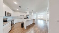 Located at 2120 Griffon Rd in Vero Beach, Florida, this well-appointed two-bedroom, two-bathroom single-floor residence offers a thoughtfully designed layout with modern finishes throughout. The open-concept kitchen and living area serves as the heart of the home, anchored by a substantial center island topped with granite countertops. Crisp white shaker cabinetry with gold-tone hardware, stainless steel appliances, and stylish pendant lighting complete the kitchen's contemporary look. Warm wood-look flooring flows through the main living areas, while a ceiling fan and large windows invite abundant natural light and outdoor views into the living room. Both bedrooms feature plush carpeting, ceiling fans, and generous windows with views of the surrounding landscape. The primary bedroom connects to a spacious en-suite bathroom showcasing a dual-sink granite vanity, a glass-enclosed walk-in shower, and direct access to a walk-in closet with wire shelving. The second bathroom mirrors the same refined aesthetic with a granite vanity and wood-look flooring. Two dedicated closets provide ample storage. The clean, neutral palette and consistent use of quality materials create a bright, cohesive ambiance throughout the entire residence.
