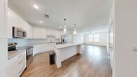 Located at 2120 Griffon Rd in Vero Beach, Florida, this well-appointed two-bedroom, two-bathroom single-floor residence offers a thoughtfully designed layout with modern finishes throughout. The open-concept kitchen and living area serves as the heart of the home, anchored by a substantial center island topped with granite countertops. Crisp white shaker cabinetry with gold-tone hardware, stainless steel appliances, and stylish pendant lighting complete the kitchen's contemporary look. Warm wood-look flooring flows through the main living areas, while a ceiling fan and large windows invite abundant natural light and outdoor views into the living room. Both bedrooms feature plush carpeting, ceiling fans, and generous windows with views of the surrounding landscape. The primary bedroom connects to a spacious en-suite bathroom showcasing a dual-sink granite vanity, a glass-enclosed walk-in shower, and direct access to a walk-in closet with wire shelving. The second bathroom mirrors the same refined aesthetic with a granite vanity and wood-look flooring. Two dedicated closets provide ample storage. The clean, neutral palette and consistent use of quality materials create a bright, cohesive ambiance throughout the entire residence.