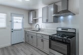 Located at 870 S Philadelphia St, Unit B in Anaheim, CA, this 2-bedroom, 1-bathroom single-story unit offers a clean, modern aesthetic throughout. Light wood-look flooring runs continuously across all rooms, complementing the bright white walls and creating a cohesive, airy feel.

The kitchen is a standout feature, equipped with gray shaker-style cabinetry, stone-look countertops, a stainless steel gas range, and a sleek wall-mounted range hood. A single-basin sink with a matte black faucet sits beneath a window, allowing natural light to fill the space. A back door provides convenient outdoor access.

The living room is bright and open, with a window dressed in white blinds and recessed lighting overhead. Both bedrooms continue the light flooring and neutral palette, each featuring ceiling fans with integrated lighting and windows that bring in natural light. One bedroom includes a closet, offering practical storage.

The bathroom is finished in crisp white tile, with a full shower-over-tub combination, a window for ventilation, and white cabinetry with black hardware accents. A hallway connects the main living areas efficiently.

An aerial view of the layout reveals a generous grassy outdoor area adjacent to the unit, providing a private retreat. The overall design is clean, functional, and well-maintained throughout.