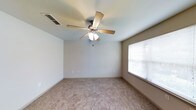 This two-floor space offers a clean and functional design with neutral interiors throughout. The pictured room showcases wall-to-wall carpeting in a warm beige tone, providing a comfortable underfoot feel and a soft, inviting atmosphere. The room is finished with smooth, light-colored walls and white baseboards, contributing to a bright and airy aesthetic.

A centrally mounted ceiling fan with a built-in light fixture serves as both a practical and subtle focal point overhead, supporting air circulation and supplemental lighting. A window fitted with horizontal blinds allows for natural light to filter into the space while offering privacy control. The overall layout of the room is open and unobstructed, lending itself well to flexible furniture arrangements.

The neutral color palette and understated finishes found throughout create a versatile backdrop that can accommodate a range of interior styles. Spanning two floors, the property offers separation between living areas, providing functional zoning within the overall layout. The combination of carpeted flooring, ceiling fans, and natural light gives the space a comfortable, livable character.
