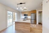 Located on University Avenue NW in Edmonton, Alberta, this well-designed one-bedroom, one-bathroom unit offers a thoughtfully efficient layout spread across a single floor. The entrance hallway, finished with light wood-look flooring and crisp white walls, leads into the heart of the unit and sets a clean, modern tone throughout.

The combined kitchen and living area serves as the centrepiece of the space. The kitchen is particularly well-appointed, featuring warm wood cabinetry extending to the ceiling, a marble-look quartz countertop island with an undermount sink, and a full suite of stainless steel appliances including a French door refrigerator, electric range, built-in microwave, and dishwasher. Pendant and track lighting add a stylish finishing touch. A sleek barn-style sliding door separates the living area from the kitchen, adding a contemporary architectural detail.

The bedroom is bright and airy, benefiting from a window with natural views of the surrounding greenery. Light wood flooring continues throughout, complementing the neutral palette. A walk-in closet provides practical storage adjacent to the bedroom.

The bathroom is clean and functional, featuring a full soaker tub with tiled surround and modern chrome fixtures. Throughout the unit, recessed lighting, white walls, and consistent flooring create a cohesive, modern aesthetic ideal for comfortable urban living.