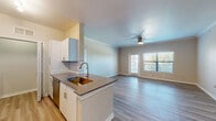 This single-floor residence offers a thoughtfully designed open-concept layout that seamlessly connects the kitchen and living areas. The kitchen is a standout feature, showcasing white cabinetry, a classic subway tile backsplash, dark quartz countertops, a brushed gold undermount sink, and a full suite of stainless steel appliances including a refrigerator, range, microwave, and dishwasher. A peninsula counter separates the kitchen from the main living area, providing both additional workspace and a natural division between the two spaces. The living area is bright and airy, benefiting from large windows with blinds that allow ample natural light to fill the room. A ceiling fan is centrally mounted, adding both function and comfort. Crown molding adds a refined touch to the living space. Light wood-style flooring flows consistently throughout the residence, lending a clean and cohesive aesthetic. The bedroom is well-proportioned, featuring a ceiling fan, a large window with outdoor views, and access to a walk-in closet. The bathroom is clean and functional, complete with a tiled soaking tub and shower combination, vanity with storage, and wood-style flooring that continues from the rest of the home.