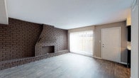 This two-story, 4-bedroom, 2-bathroom home offers a well-organized layout across two levels. The main floor centers around a generously sized living room distinguished by a floor-to-ceiling dark brick fireplace that serves as a dramatic focal point. Large vertical-blind-covered windows flood the space with natural light, while dark hardwood-style flooring extends throughout the main living areas. An open staircase with clean railings connects the main floor to the upper level, adding an architectural element to the common spaces. Adjacent to the living room, a dedicated dining area features a chandelier overhead and continues the same rich hardwood-style flooring. The galley-style kitchen is outfitted with dark cabinetry, light quartz-style countertops, a tile backsplash, and white appliances. The bathrooms include tub-shower combinations with large-format tile surrounds and matching dark vanity cabinetry. The four bedrooms are located upstairs, each featuring plush carpeting, ceiling fans with light fixtures, and closets. Neutral-toned walls throughout provide a clean, cohesive backdrop across the entire home.