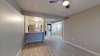 This single-floor residence offers a clean, functional layout with consistent light wood-tone vinyl flooring running throughout every room, providing a cohesive and low-maintenance living environment. The open living area serves as the heart of the home, featuring a ceiling fan, a large window fitted with horizontal blinds that allows natural light to fill the space, and a front entry door. The layout flows directly into the kitchen and hallway beyond.

The kitchen is efficiently designed with white upper cabinetry, gray lower cabinets, white subway tile backsplash, and bright white countertops. Stainless steel appliances — including a refrigerator, electric range, and over-the-range microwave — provide a modern finish. An electrical panel is integrated into the kitchen wall, and a peninsula counter separates the kitchen from the living area.

Adjacent to the kitchen, an in-unit laundry area accommodates a stacked or side-by-side washer and dryer setup. A hallway connects the main living space to the private areas of the home, which include two bedrooms. Each bedroom is finished in neutral warm-gray tones with vinyl flooring and windows with blinds offering natural light. The full bathroom features a single-sink vanity with a framed mirror, a toilet, and a shower-tub combination with a clean white surround.
