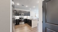 This thoughtfully designed single-floor residence offers a seamless open-concept layout that connects the kitchen, dining, and living areas into one cohesive, light-filled space. The gourmet kitchen is a standout feature, showcasing dark shaker-style cabinetry with brushed nickel hardware, granite countertops, a classic white subway tile backsplash, stainless steel appliances including a range, microwave, and refrigerator, and a peninsula with an undermount sink — ideal for both cooking and entertaining. Warm wood-tone flooring runs consistently throughout the unit, enhancing the sense of continuity and flow. The living area is bright and inviting, benefiting from natural light that streams in through large windows with views of greenery outside, and opens to an outdoor balcony access door. The bedrooms are calm and serene, each featuring large windows, neutral wall tones, and ample space. The bathroom mirrors the kitchen's design aesthetic with matching dark cabinetry, granite countertops, a large vanity mirror, and bold dark paneled doors that add a dramatic architectural touch. Recessed lighting throughout maintains a clean, modern ceiling profile, while the neutral color palette and curated design details create a polished and cohesive ambiance from room to room.