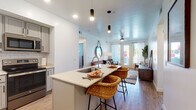 This single-floor unit offers a well-designed, open-concept layout that seamlessly connects the kitchen and living areas. The kitchen is a standout feature, equipped with gray shaker-style cabinetry, a subway tile backsplash, stainless steel appliances, and a spacious center island with a built-in sink and seating for two. Pendant lighting and recessed fixtures illuminate the space, while a dedicated walk-in pantry provides generous storage.

The living area is bright and welcoming, featuring wood-look flooring, a ceiling fan, and French doors that open to an outdoor space, allowing natural light to flow freely throughout. The bedroom continues the comfortable aesthetic with plush carpeting, a ceiling fan, and a window dressed with sheer curtains and blinds.

A dedicated office or flex room offers carpeted flooring and a window with blackout curtains, providing a functional workspace. Two bathrooms serve the unit — one featuring wood-look tile flooring, gray vanity cabinetry, and a tub-shower combination, while the second bathroom mirrors a similarly clean, neutral design. Throughout the unit, white walls and consistent finishes contribute to a cohesive, modern ambiance.