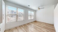 This single-floor space showcases a clean, contemporary design with a cohesive aesthetic carried throughout. Light hardwood flooring extends across all areas, creating a warm and unified foundation that complements the crisp white walls and trim found in every room.

The main living area is generously proportioned and benefits from an impressive bank of large windows fitted with horizontal blinds, allowing abundant natural light to fill the space. Urban views of the surrounding neighborhood are visible through the windows. A ceiling fan provides additional comfort and airflow overhead.

The galley-style kitchen is well-appointed with white shaker cabinetry, granite countertops, a subway tile backsplash, and a full suite of stainless steel appliances including a refrigerator, range, microwave, and dishwasher. Built-in open shelving adds functional storage. A barn-style sliding door and recessed lighting contribute to the kitchen's modern character, while a window at the end draws in natural light.

The bathroom features floor-to-ceiling grey tile surrounding a full soaking tub and shower, a white vanity with granite countertop, and continued hardwood-style flooring. Throughout, the space maintains a bright, minimalist ambiance with thoughtful finishes.
