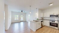 Located at 14055 Central Loop in Woodbridge, VA, this 2-bedroom, 2-bathroom residence offers a well-designed single-level layout with a bright, open feel throughout. The combined kitchen and living area serves as the heart of the home, featuring light hardwood-style flooring, white walls, and a ceiling fan that enhance the airy atmosphere. Large windows and a glass-paneled balcony door flood the space with natural light and provide outdoor views of the surrounding landscaped community.

The kitchen is well-appointed with crisp white shaker-style cabinetry, granite-look countertops, a center island with a sink, stainless steel appliances including a French door refrigerator, range, microwave, and dishwasher, and stylish pendant lighting overhead. The balcony offers a peaceful outdoor retreat overlooking the community grounds.

Both bedrooms are comfortably sized with light flooring, neutral walls, and natural light from windows with blinds. The primary bedroom is a well-proportioned retreat, and the unit includes four closets in total—some featuring wire shelving systems for organized storage. The two bathrooms are clean and functional, with one including a shower/tub combination. An in-unit laundry area adds everyday convenience to this thoughtfully laid-out home.