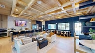Located at 7135 Mount Zion Circle in Morrow, Georgia, this single-floor communal space offers a thoughtfully designed environment that blends modern aesthetics with warm, inviting materials. The standout architectural feature is the stunning coffered wood ceiling, which spans the entire space and adds richness and texture overhead, complemented by wide-plank light hardwood flooring throughout.

The kitchen is outfitted with sleek light wood cabinetry, a large waterfall-edge marble-look island with bar seating, stainless steel appliances including a double wall oven and French door refrigerator, and a wall-mounted flat-screen TV above the countertop. Elegant globe pendant lights in brushed gold add a refined touch.

The dining area flows seamlessly from the kitchen into an open-concept lounge and gathering zone, anchored by bold navy blue accent walls and built-in open shelving styled with decorative objects. Comfortable lounge seating is arranged around a central coffee table, creating an inviting social setting. Floor-to-ceiling glass doors and windows flood the space with natural light and offer views of the outdoor surroundings. The overall ambiance is upscale yet approachable, ideal for community gatherings and everyday use.