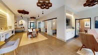 Located at 1800 Silas Deane Highway in Rocky Hill, Connecticut, this thoughtfully designed communal space offers a well-appointed, single-floor layout that balances collaborative and private work environments. The main gathering area serves as the centerpiece, featuring a large live-edge wood communal table surrounded by mixed seating and anchored by a herringbone wood-inlay area rug over large-format tile flooring. Eye-catching hexagonal pendant light fixtures in warm wood tones hang overhead, adding an artful, organic touch to the modern interior. Natural light filters in through full-height glass entry doors and surrounding windows, creating a bright and welcoming ambiance throughout. A kitchenette area is outfitted with white cabinetry, a stainless steel sink, and a striking backlit hexagonal tile backsplash, accompanied by casual banquette seating and bistro-style tables ideal for informal gatherings. Sliding glass doors reveal a private conference room furnished with a round marble-top table, upholstered chairs, a wall-mounted display screen, and a statement pendant light fixture — designed for focused meetings or small group sessions. Compact individual work pods, each equipped with a built-in wood desk, task lighting, and patterned carpet, provide quiet spaces for heads-down productivity. Together, these distinct zones create a versatile, design-forward space suited for both community and focused work.