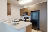 Located at 3534 E Capitol St NE in Washington, DC, this 2-bedroom, 2-bathroom unit offers a thoughtfully designed single-floor layout. The open-concept living, dining, and kitchen area serves as the heart of the home, featuring light wood-style flooring that creates a clean, modern aesthetic. The kitchen is well-appointed with warm wood-tone cabinetry, ample upper and lower storage, a peninsula with a built-in sink and white countertops, and black appliances including a refrigerator, range, and microwave. Natural light fills the space from multiple windows fitted with horizontal blinds. Both bedrooms are carpeted for comfort and include large windows that bring in generous daylight. Three closets provide ample storage throughout the unit. The two bathrooms are finished with large-format gray tile flooring and warm wood vanities; one bathroom features a full tub-shower combination, while the other offers a walk-in style closet with wire shelving. A dedicated laundry area adds everyday convenience, and a connecting hallway ties the layout together efficiently. The overall design presents a contemporary and functional living space suited for a range of lifestyles.