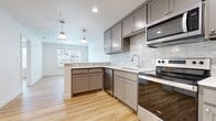 This thoughtfully designed 1-bedroom, 1-bathroom residence offers a cohesive and modern living experience across a single floor. The open-concept layout seamlessly connects the kitchen and living room, creating an inviting, airy atmosphere ideal for both everyday living and entertaining. The kitchen is a standout feature, outfitted with gray shaker-style cabinetry, a subway tile backsplash, stainless steel appliances including a refrigerator, electric range, microwave, and dishwasher, and a peninsula that provides additional prep and seating space. Pendant lighting above the peninsula adds a stylish touch. Light hardwood flooring flows consistently throughout the entire residence, enhancing the sense of continuity and warmth. The bedroom is a comfortable, well-proportioned retreat with natural light streaming in through windows fitted with horizontal blinds. An adjacent walk-in closet offers built-in shelving and hanging rods, providing generous storage. The bathroom features a gray vanity, tile-surround shower, and hardwood flooring that carries through from the main living areas. Clean white walls, recessed lighting, and a neutral color palette throughout lend the space a fresh, modern character that is both functional and visually appealing.