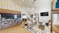 This well-appointed 3-bedroom, 2-bathroom single-story home offers a thoughtfully designed layout with striking architectural details. The open-concept living and kitchen area is anchored by dramatic vaulted ceilings that amplify the sense of space, with light wood flooring flowing seamlessly throughout. The kitchen is a standout feature, showcasing rich dark wood cabinetry, striking granite countertops with a bold veining pattern, a full granite-wrapped island with bar seating, stainless steel appliances, a statement backsplash, and a sleek matte black faucet — all framed by a warm slatted wood accent wall that extends to the ceiling. The adjacent living area is bright and airy, benefiting from large windows that invite natural light, and is finished with a ceiling fan overhead. The three bedrooms are generously proportioned, each featuring soaring ceilings, double-door closets with gray hardware, and light-filled windows. The primary bathroom impresses with a dual vessel sink vanity, granite countertops, dark wood cabinetry, and a tiled walk-in shower, while the secondary bathroom offers a clean, minimalist design with a natural window. A connecting hallway completes the efficient, single-level floor plan.