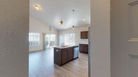 Located at 18417 E Appleway Ave in Spokane Valley, WA, this thoughtfully designed unit offers a single-level layout with an open, airy feel defined by striking vaulted ceilings that amplify the sense of space throughout. The open-concept kitchen serves as the heart of the home, showcasing rich dark-toned cabinetry, a large center island with a built-in sink and light countertops, stainless steel appliances including a range, microwave, and refrigerator, and stylish pendant lighting that adds a warm, modern touch. Light wood-style flooring runs throughout the main living areas, complementing the neutral color palette and contributing to the bright, clean aesthetic. The living area is generously proportioned, benefiting from abundant natural light through large windows and sliding glass door access to a private balcony with outdoor views. A dedicated bedroom features plush carpeting, soaring ceilings, a wall-mounted mini-split system for personalized climate control, and its own balcony access. The bathroom is well-appointed with dark cabinetry, light countertops, a full tub-shower combination, and a window for natural light. Overall, the unit presents a fresh, contemporary ambiance with quality finishes and functional design throughout.