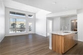 Located at 3852 E Warm Springs Ave in Boise, Idaho, this single-floor unit presents a contemporary design with a bright, open-concept layout. Light wood-tone flooring runs throughout the main living areas, complementing the crisp white walls and modern finishes that define the overall aesthetic.

The kitchen is a standout feature, showcasing a two-tone design with warm wood lower cabinetry and white upper cabinets. A large island with a striking veined quartz countertop provides both workspace and seating, while stainless steel appliances—including a range, microwave, and refrigerator—complete the well-equipped space. A subway tile backsplash adds a clean, polished touch.

The living area benefits from soaring ceilings and oversized windows that invite generous natural light. A glass-paneled door opens directly onto a private balcony, offering outdoor views of the surrounding community. An additional room features plush carpeting, a walk-in closet with built-in shelving, and a window with exterior views.

The bathroom is finished with a wood-toned vanity, quartz countertop, a large mirror, and a tiled tub-shower combination. Additional rooms with light hardwood flooring offer flexible use. Throughout, the unit maintains a cohesive, modern sensibility with clean lines and neutral tones.