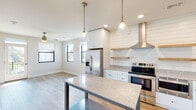 This well-designed 1-bedroom, 1-bathroom unit offers a thoughtfully arranged single-floor layout that maximizes every square foot. The open-concept kitchen serves as the centerpiece of the living area, showcasing white shaker cabinetry, granite countertops, and a full suite of stainless steel appliances including a French door refrigerator, electric range with overhead hood vent, built-in microwave, and dishwasher. A shiplap accent wall adds a modern farmhouse character, complemented by floating wood shelves and elegant pendant lighting overhead. Light wood-look flooring runs throughout the main living and kitchen areas, enhancing the bright, airy feel of the space. The bedroom is generously proportioned, featuring plush neutral carpeting, a ceiling fan, and large windows that invite abundant natural light and offer views of the surrounding neighborhood. A dedicated closet provides practical storage. The bathroom features a full tub and shower combination finished with classic white subway tile and chrome fixtures. Recessed lighting and large black-framed windows throughout the unit contribute to a clean, contemporary aesthetic that is both functional and visually appealing.