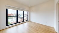 Located at 1525 N American St, Unit 606 in Philadelphia's vibrant Northern Liberties neighborhood, this two-bedroom, two-bathroom residence spans two floors with a thoughtful modern design. Light hardwood flooring flows throughout, complementing the clean white walls and contemporary finishes that define the space.

The kitchen serves as a functional centerpiece, featuring stainless steel appliances, flat-front cabinetry in a warm neutral tone, a large central island with an integrated sink, and distinctive green pendant lighting that adds a touch of personality. A staircase connects the main living area to the upper level, which includes access to a private rooftop terrace with a striking red-paneled exterior.

Both bedrooms are well-proportioned, bathed in natural light through large black-framed windows that frame expansive views of the Philadelphia skyline and surrounding neighborhood. The primary bedroom includes direct access to an en-suite bathroom. Both bathrooms are finished with warm golden tile, floating vanities, and clean modern fixtures — one featuring a dual-sink vanity with a mirrored medicine cabinet, the other a full soaking tub. The overall ambiance is bright, clean, and contemporary, offering a polished urban living experience.